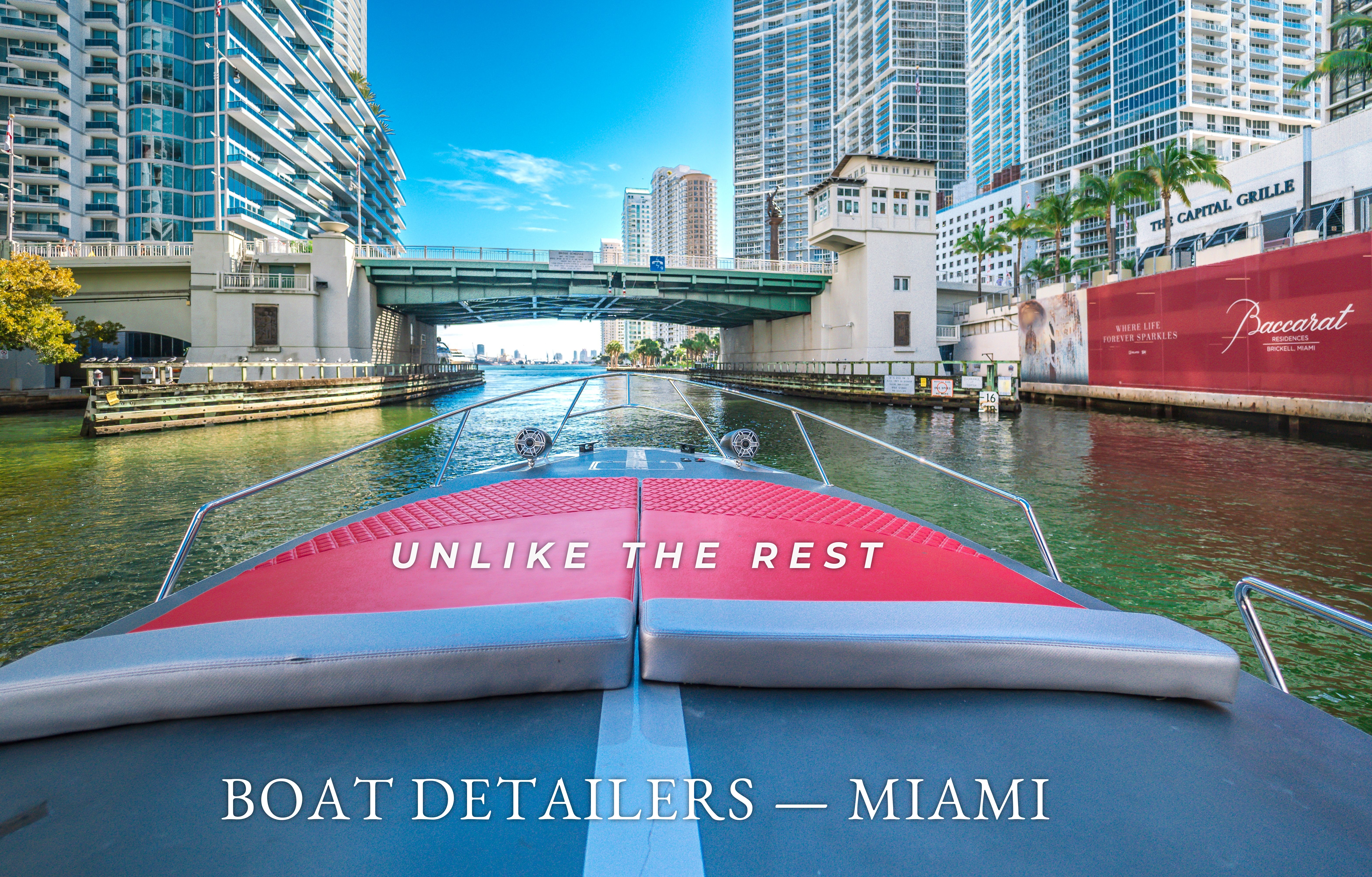 View over a detailed boat's red bow pad and grey cushions cruising the Miami River at the Brickell Avenue bridge, with downtown high-rises alongside