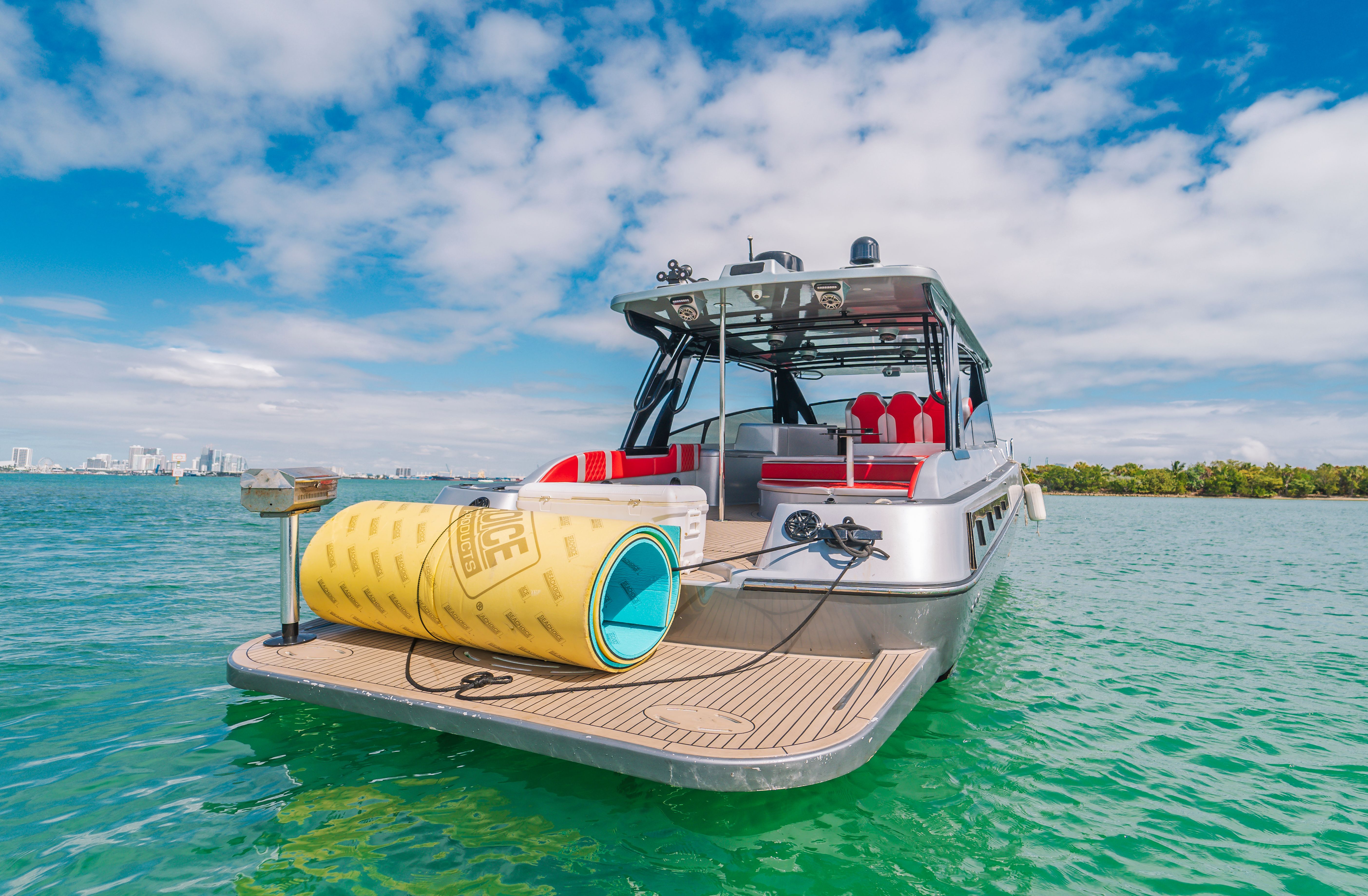 Silver center console with a teak swim platform anchored in clear green water on Biscayne Bay, Miami skyline on the horizon