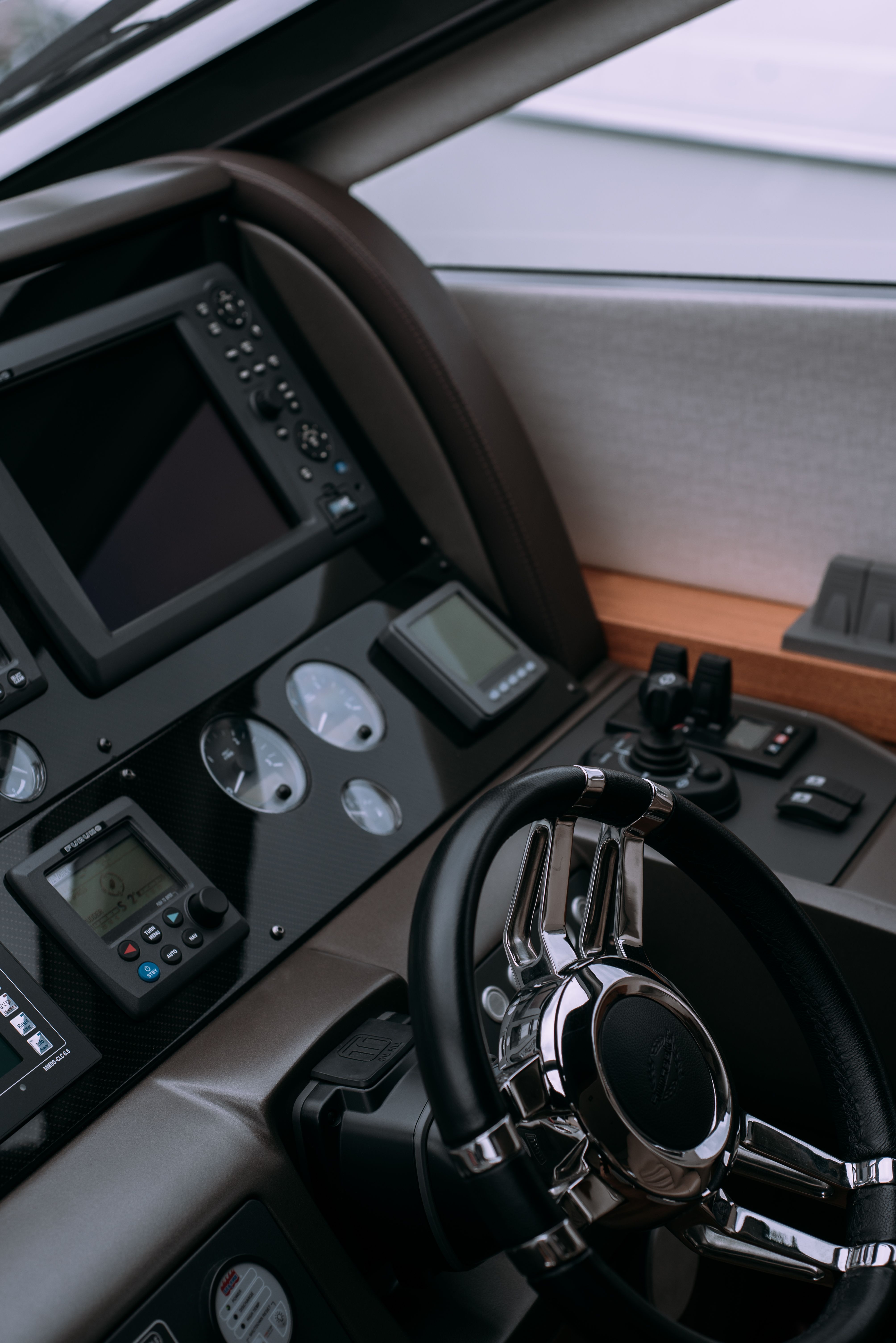 Close-up of a detailed luxury yacht helm with a black and chrome steering wheel, chartplotter and gauges