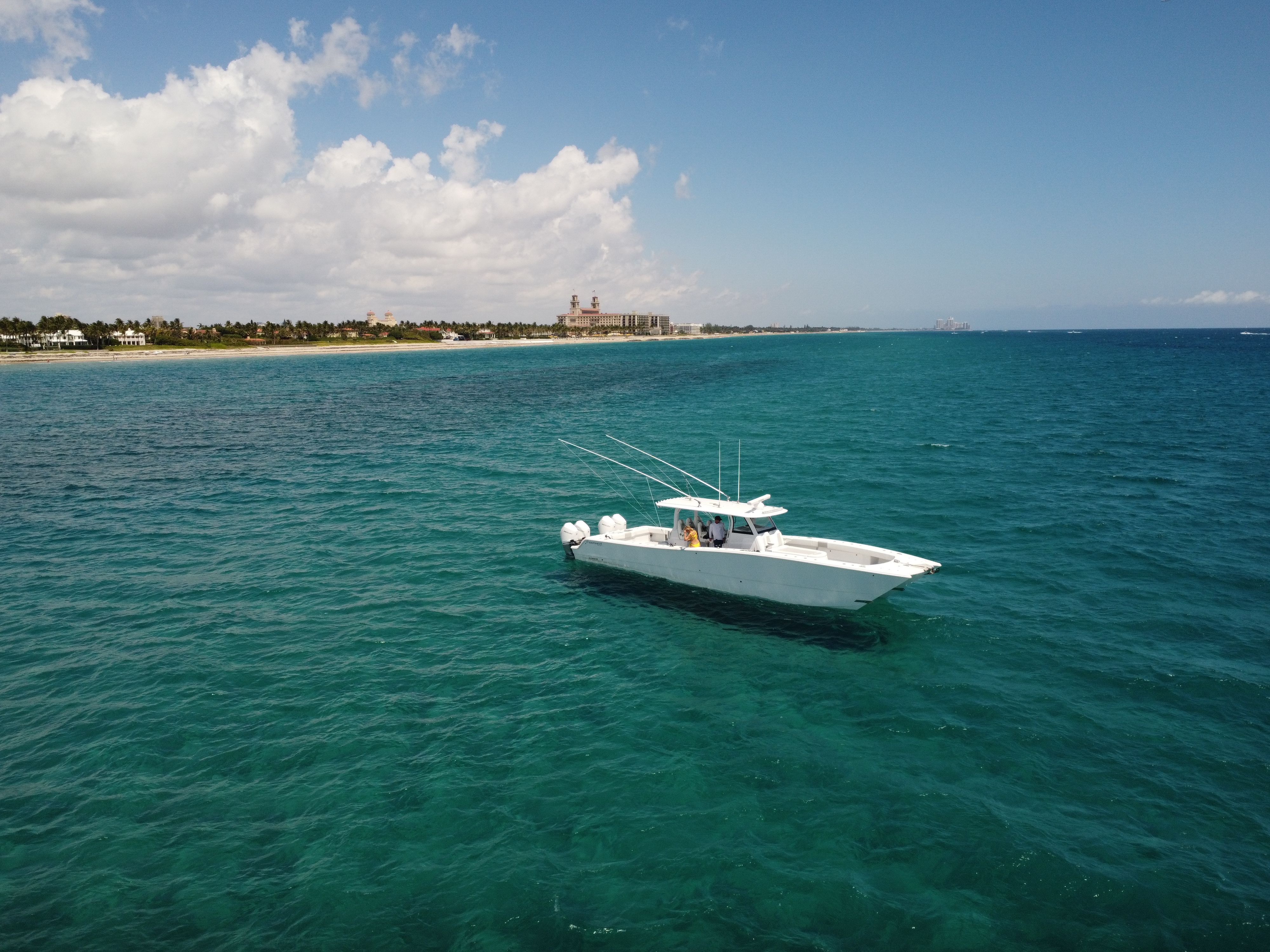 Aerial view of a white center console with quad outboard engines on turquoise water off Palm Beach, The Breakers hotel in the distance