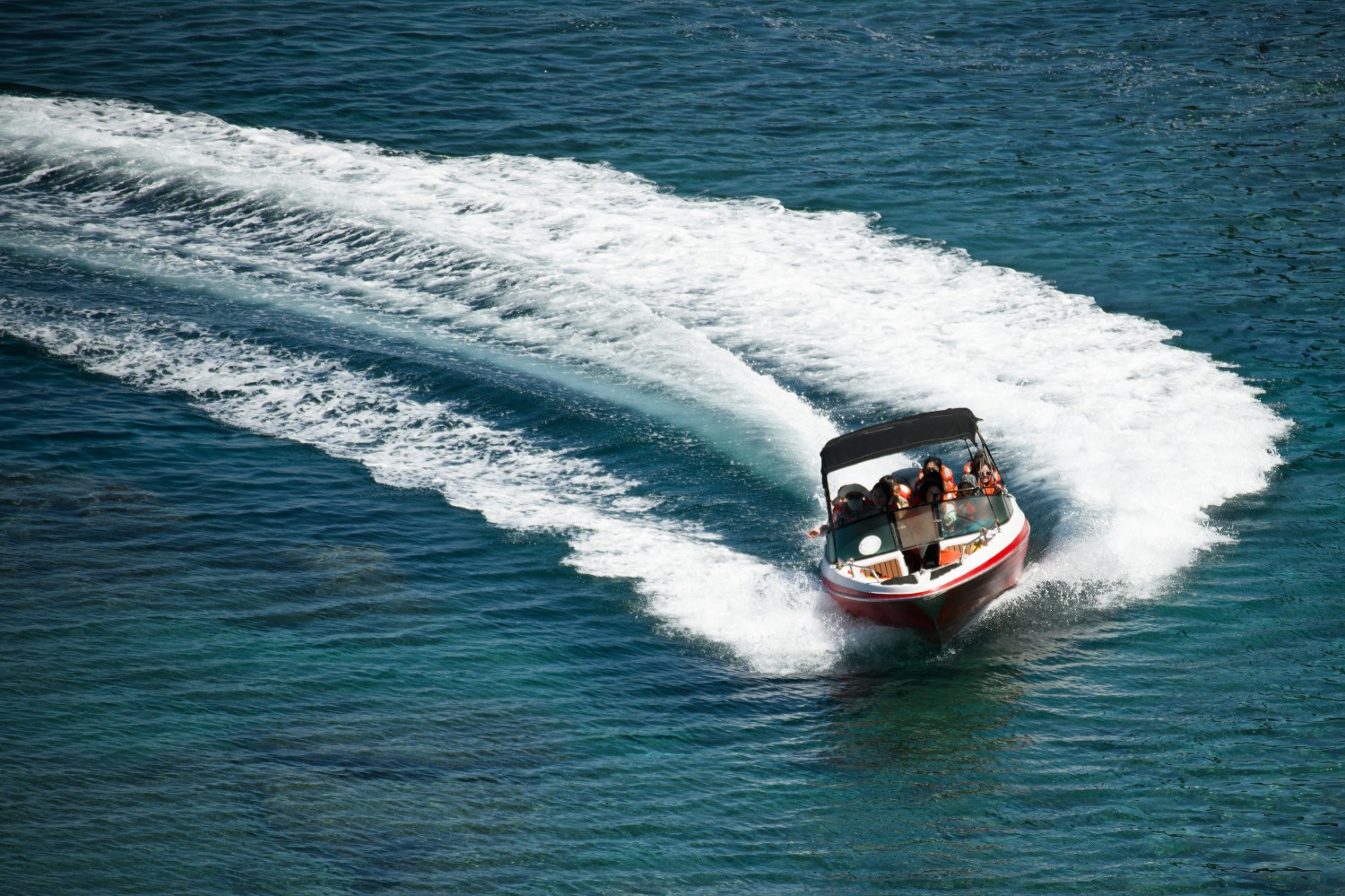 Aerial view of a red and white bowrider carving a turn and throwing a curved white wake across deep teal-blue water