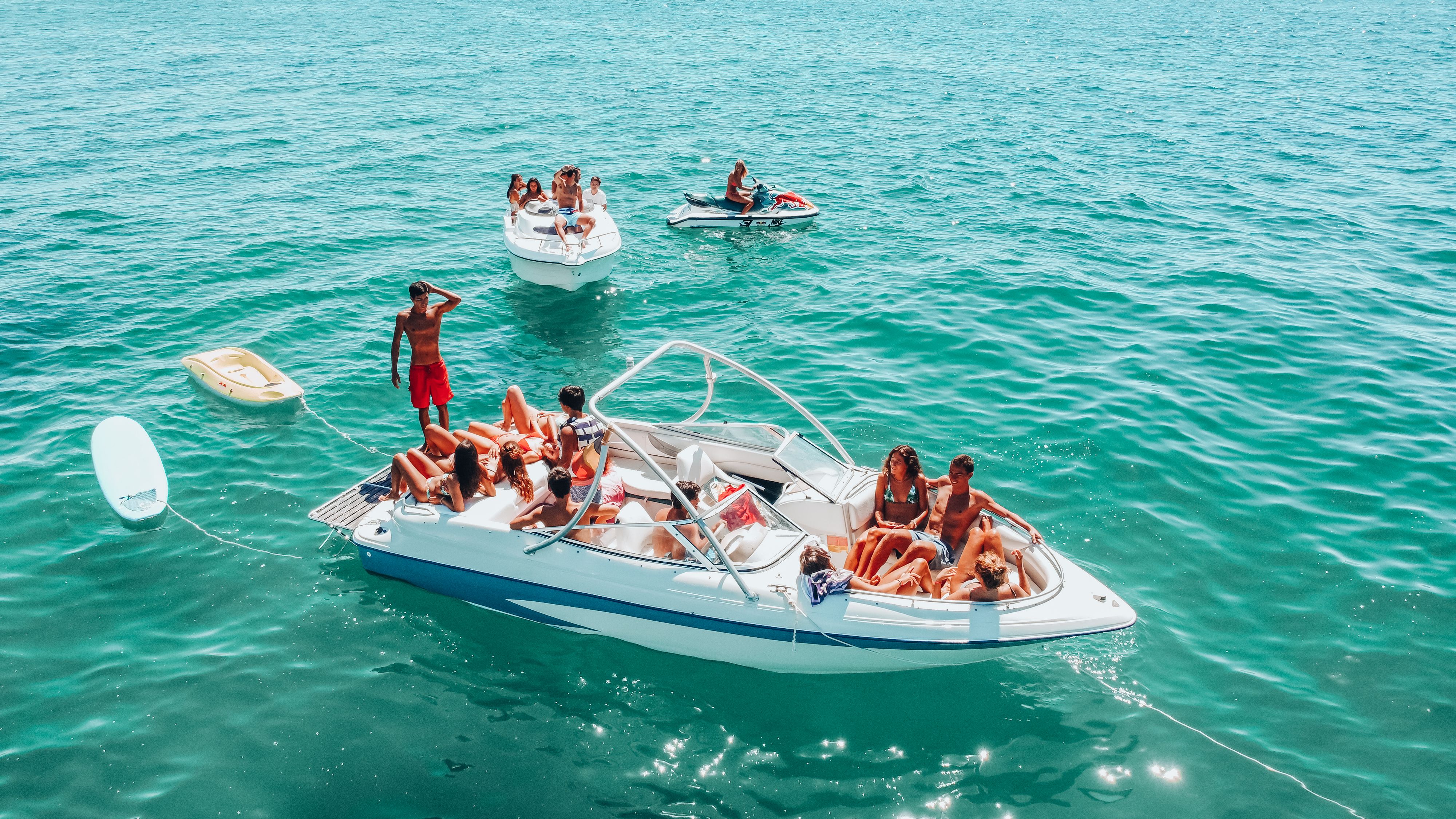 Aerial view of a bowrider full of friends at a South Florida sandbar party, surrounded by boats in bright turquoise water